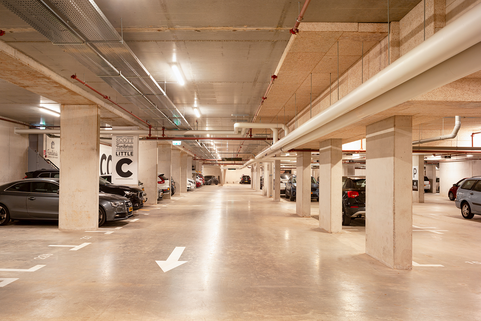 Een ruime en goed verlichte ondergrondse parkeergarage met verschillende geparkeerde auto's.