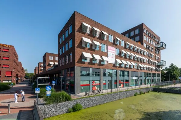 Modern kantoorpand aan de Maasstadweg met rode bakstenen gevel, witte zonwering en een vijver op de voorgrond.