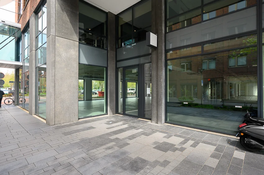 Moderne glazen gevel en entree van een kantoorpand aan de Maasstadweg met reflecties van tegenoverliggende gebouwen.
