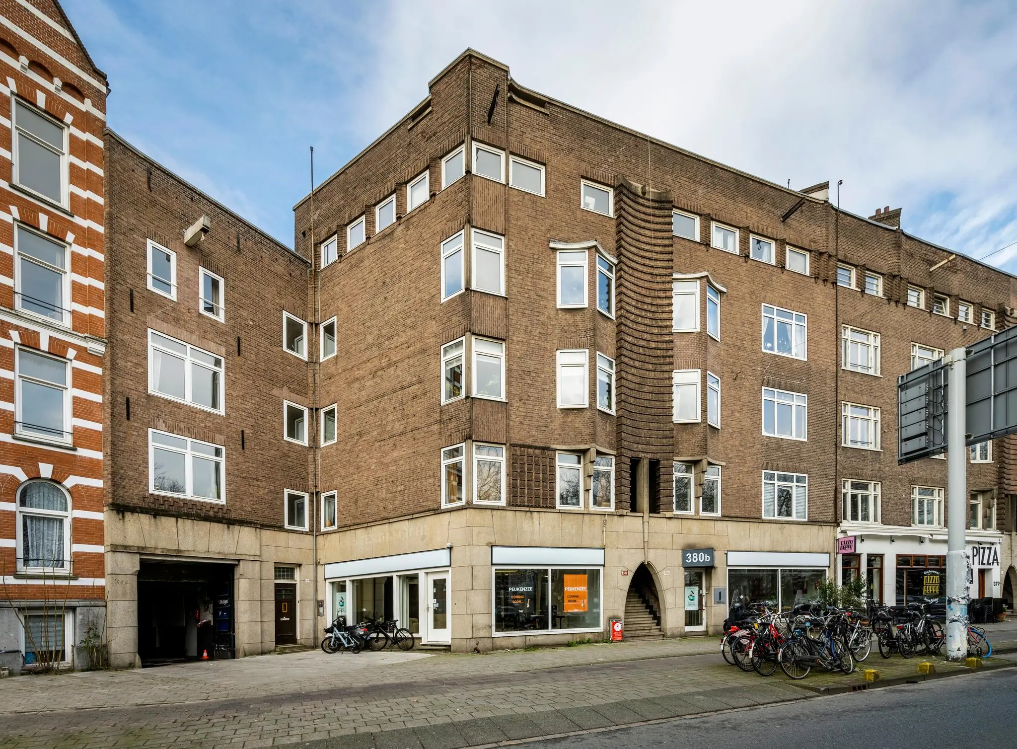Hoekpand aan de Nassaukade met bakstenen gevel, grote ramen, fietsenrekken en winkelruimtes op de begane grond.