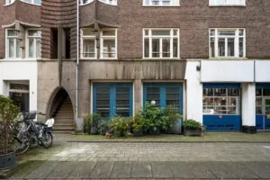 Voorgevel van een woongebouw aan de Nassaukade met blauwe deuren, plantenbakken, fietsen en een trap onder een rondboog.