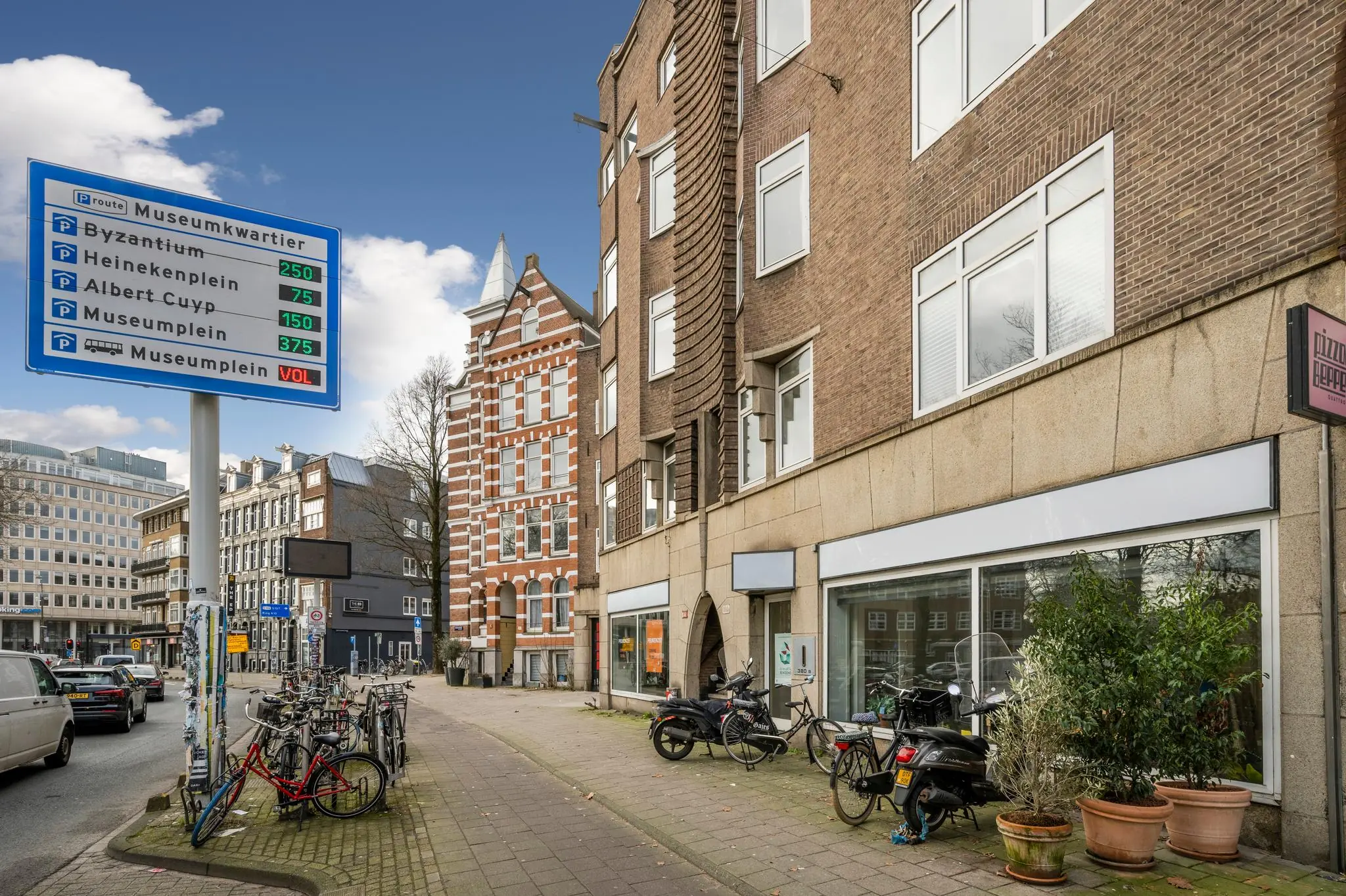 Straatbeeld van de Nassaukade in Amsterdam met fietsen, parkeerinformatie en karakteristieke gevels.