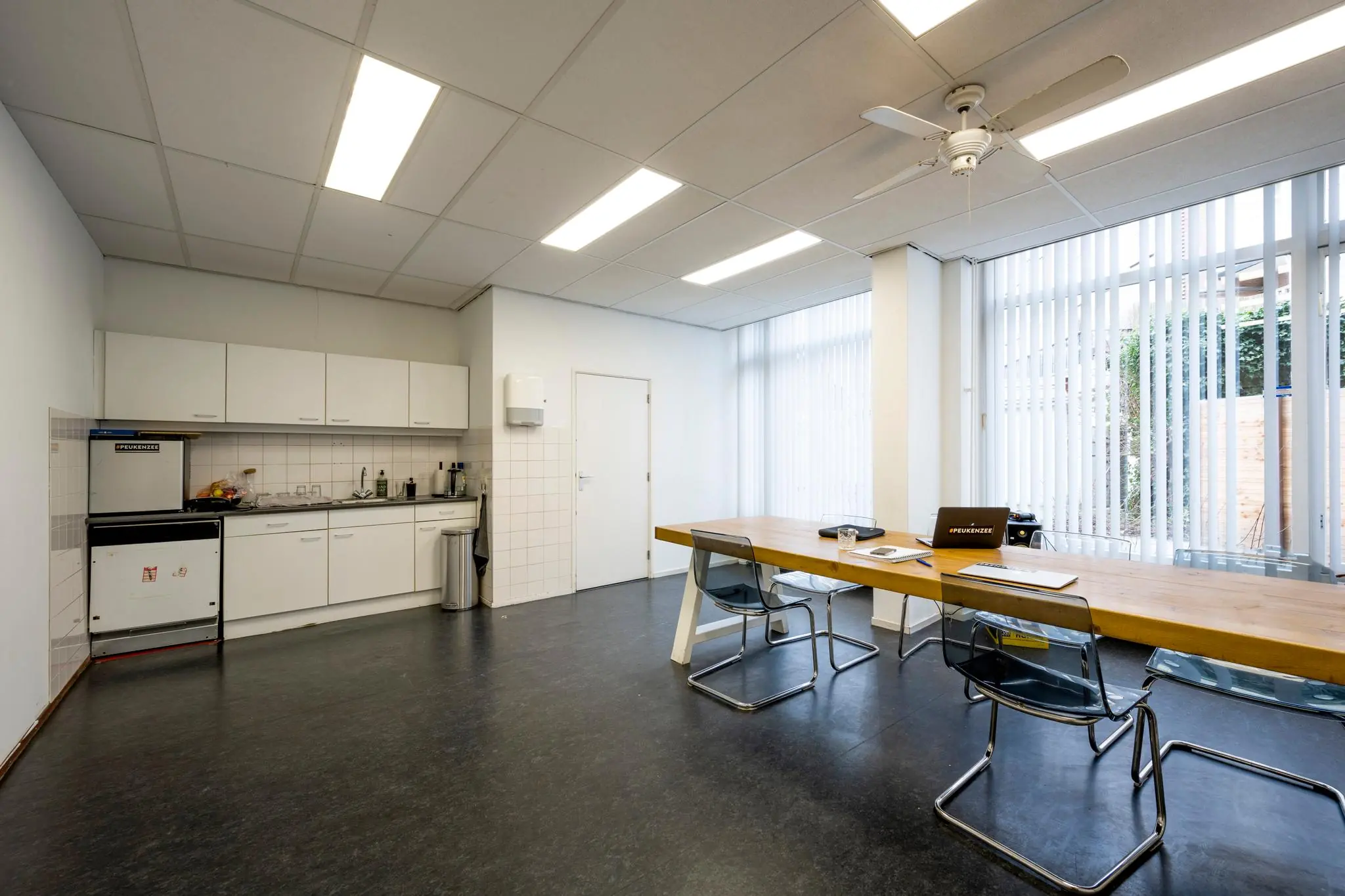 Moderne kantoorruimte aan de Nassaukade met een open keuken en vergadertafel bij grote ramen met verticale lamellen.