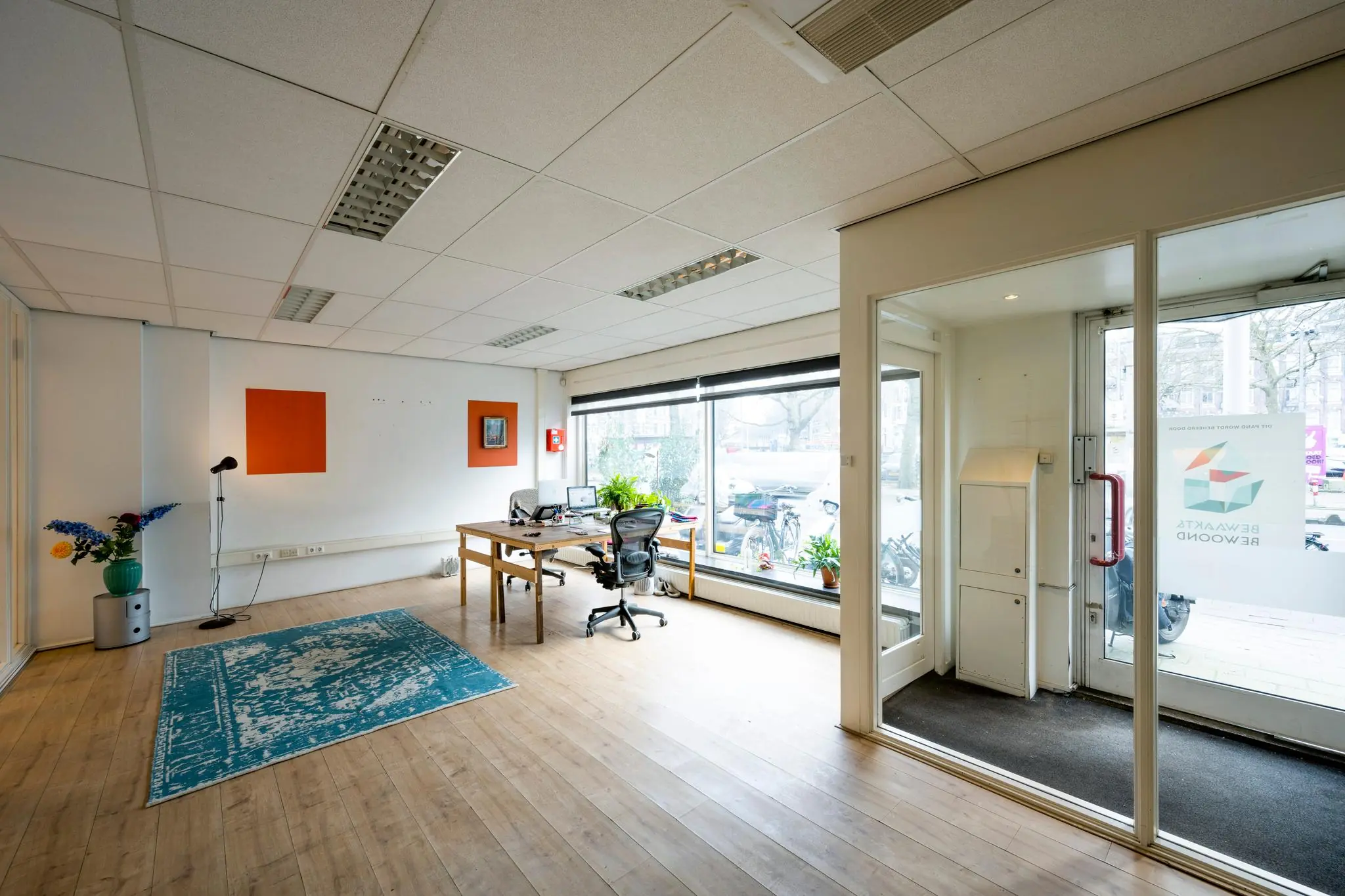 Licht en modern kantoor aan de Nassaukade met grote ramen, houten vloer en een werkplek met planten.