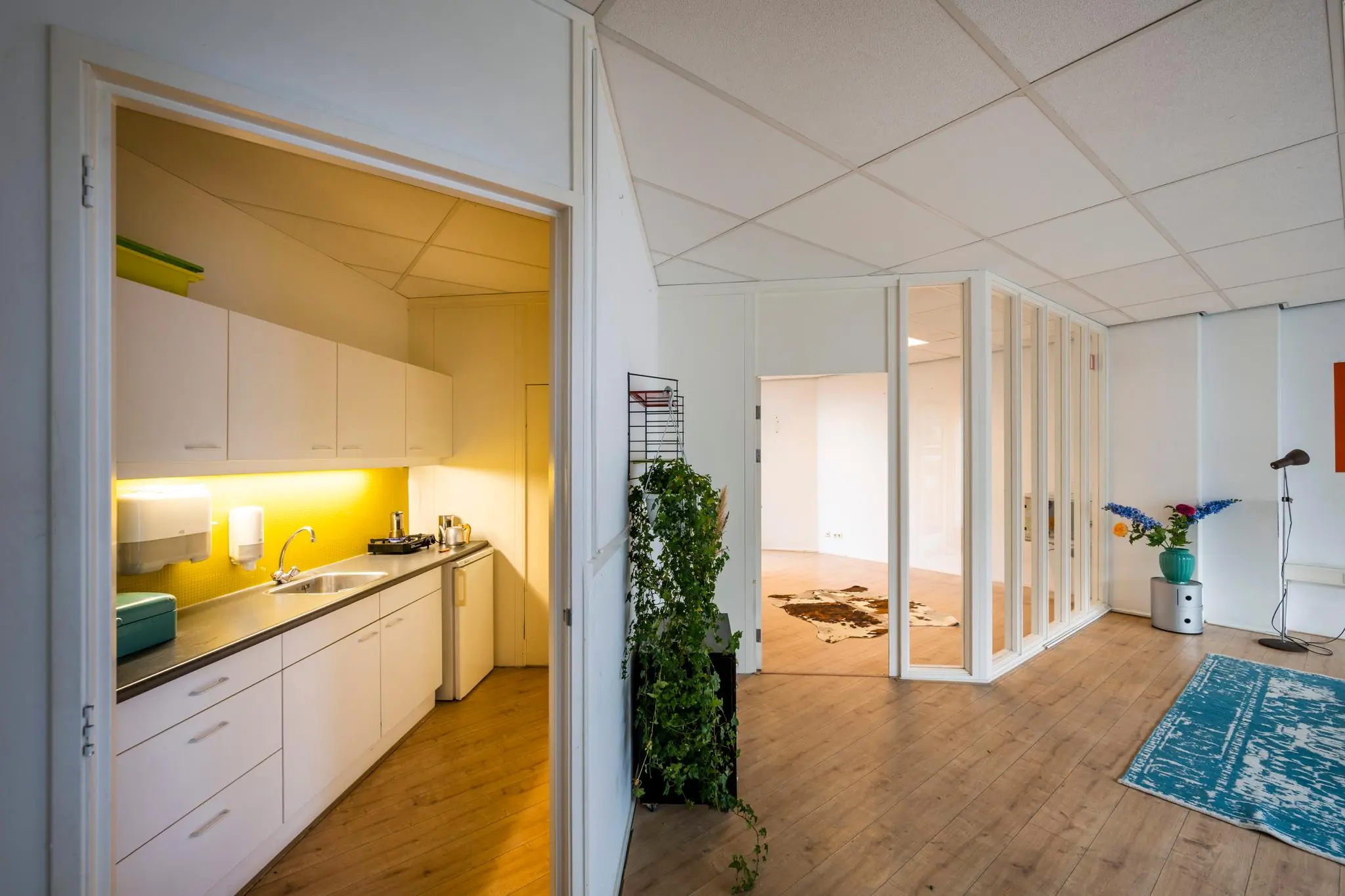 Moderne kantoorruimte aan de Nassaukade met een open keuken, glazen scheidingswand en houten vloer.