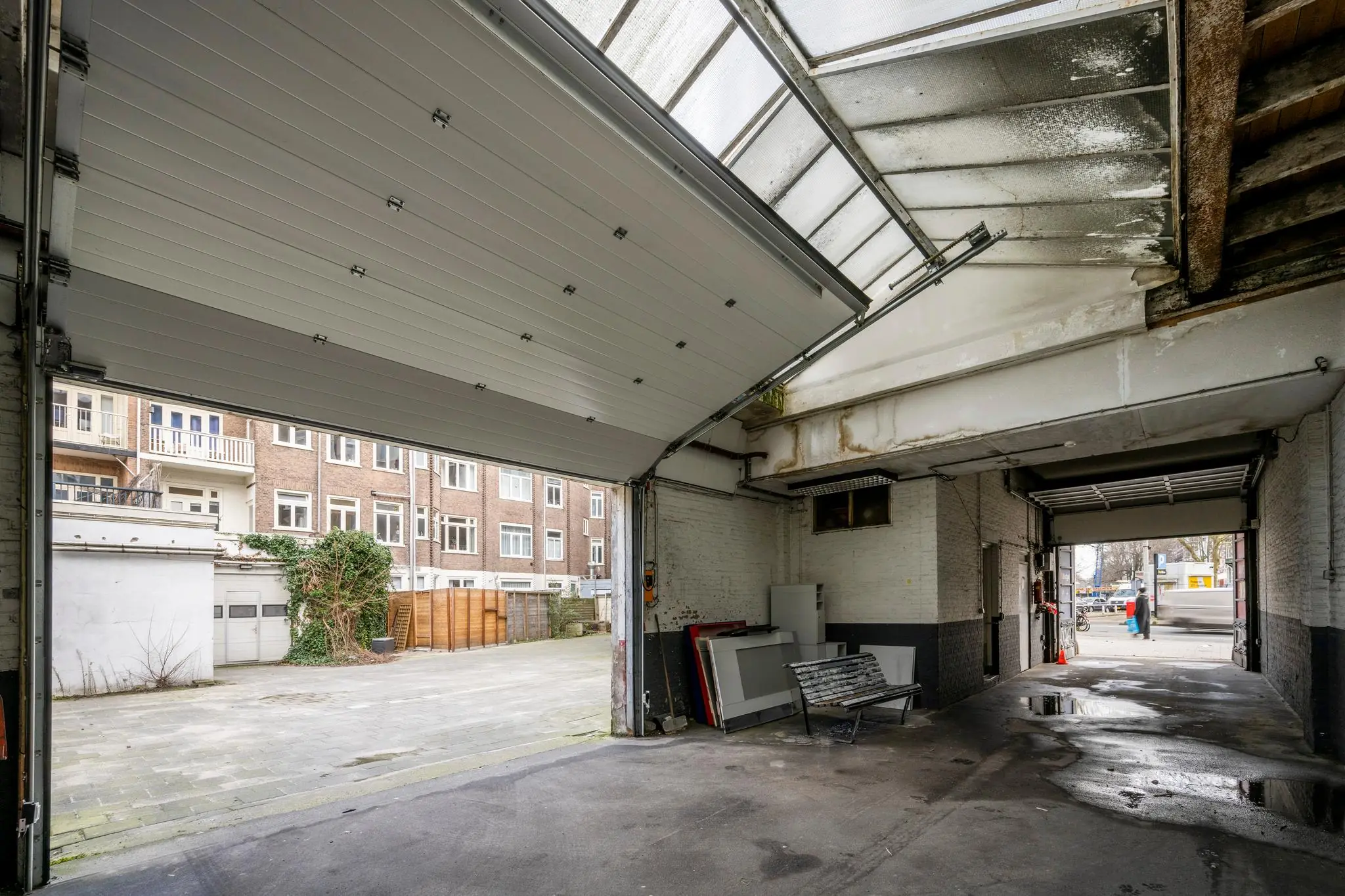 Doorkijk vanuit een garage aan de Nassaukade naar de binnenplaats en straat met deels geopende garagedeuren.