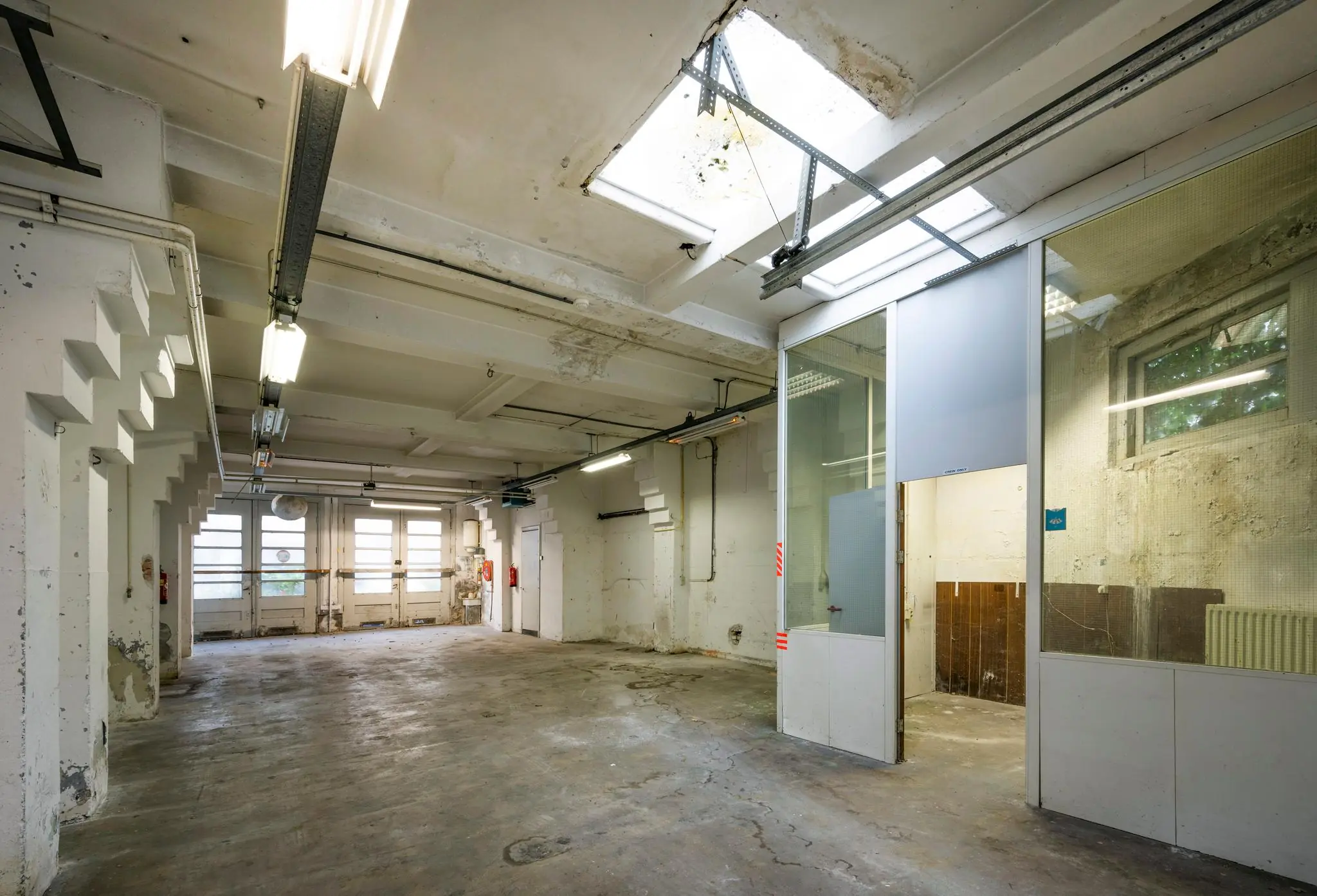Leegstaand industrieel pand aan de Nassaukade met betonnen vloer, glaswanden en tl-verlichting.