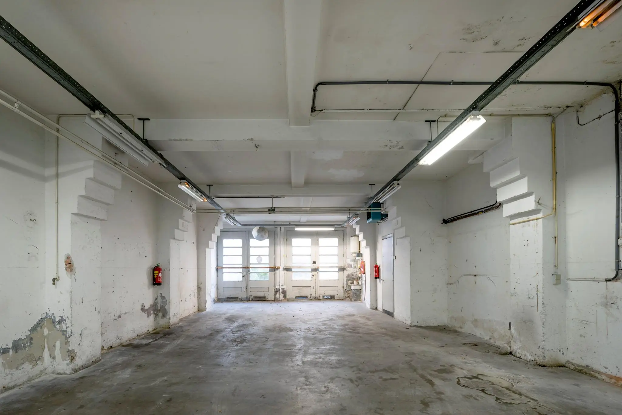 Lege, verouderde garage of opslagruimte aan de Nassaukade met betonnen vloer en witte muren.