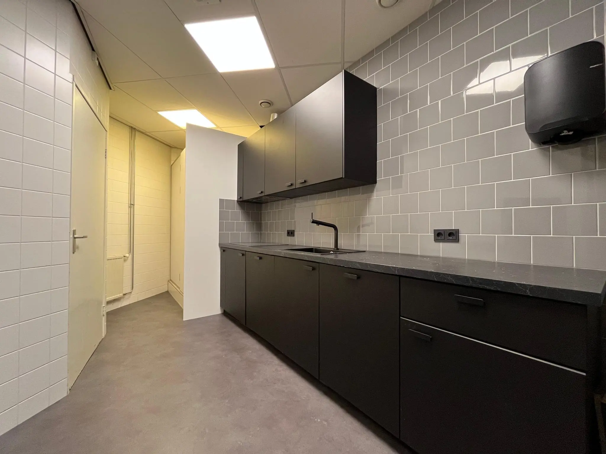 Smalle, modern ingerichte keuken met zwarte kasten en grijze tegelwand aan de Utrechtseweg.