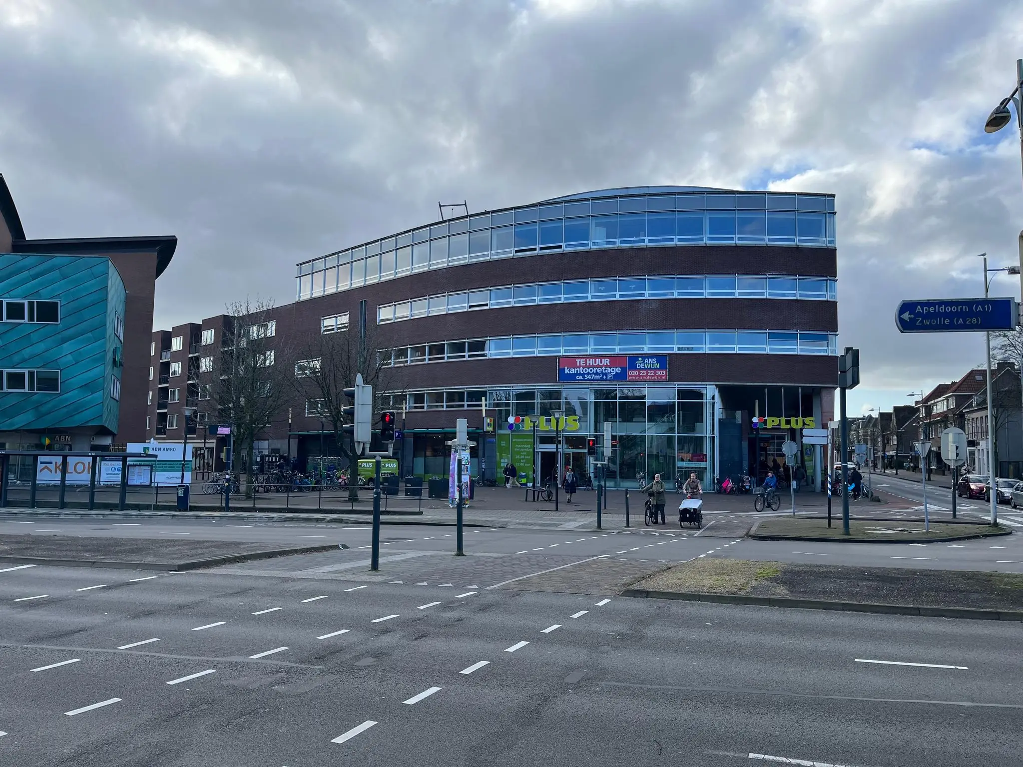 Straatbeeld van de Arnhemseweg in Apeldoorn met een PLUS-supermarkt in een modern kantoorpand op de hoek.