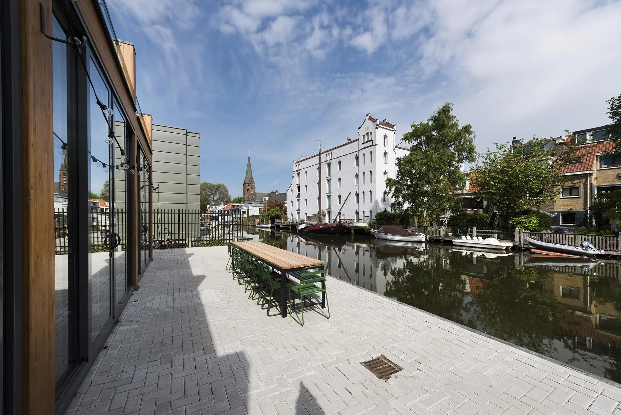 Terras met picknicktafels aan de Nieuwendammerkade met uitzicht op een gracht, boten en historische gebouwen.