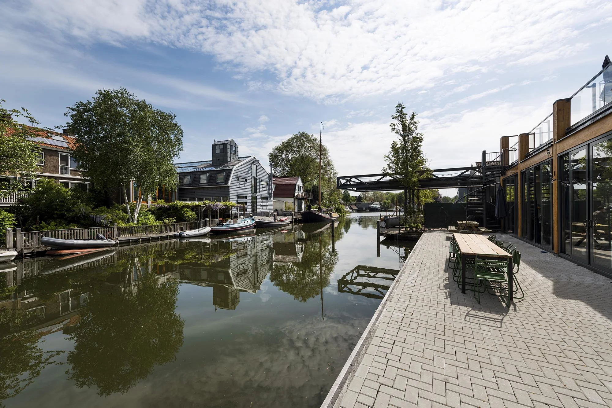 Terras aan het water aan de Nieuwendammerkade met uitzicht op woonboten, panden en een brug over het kanaal.