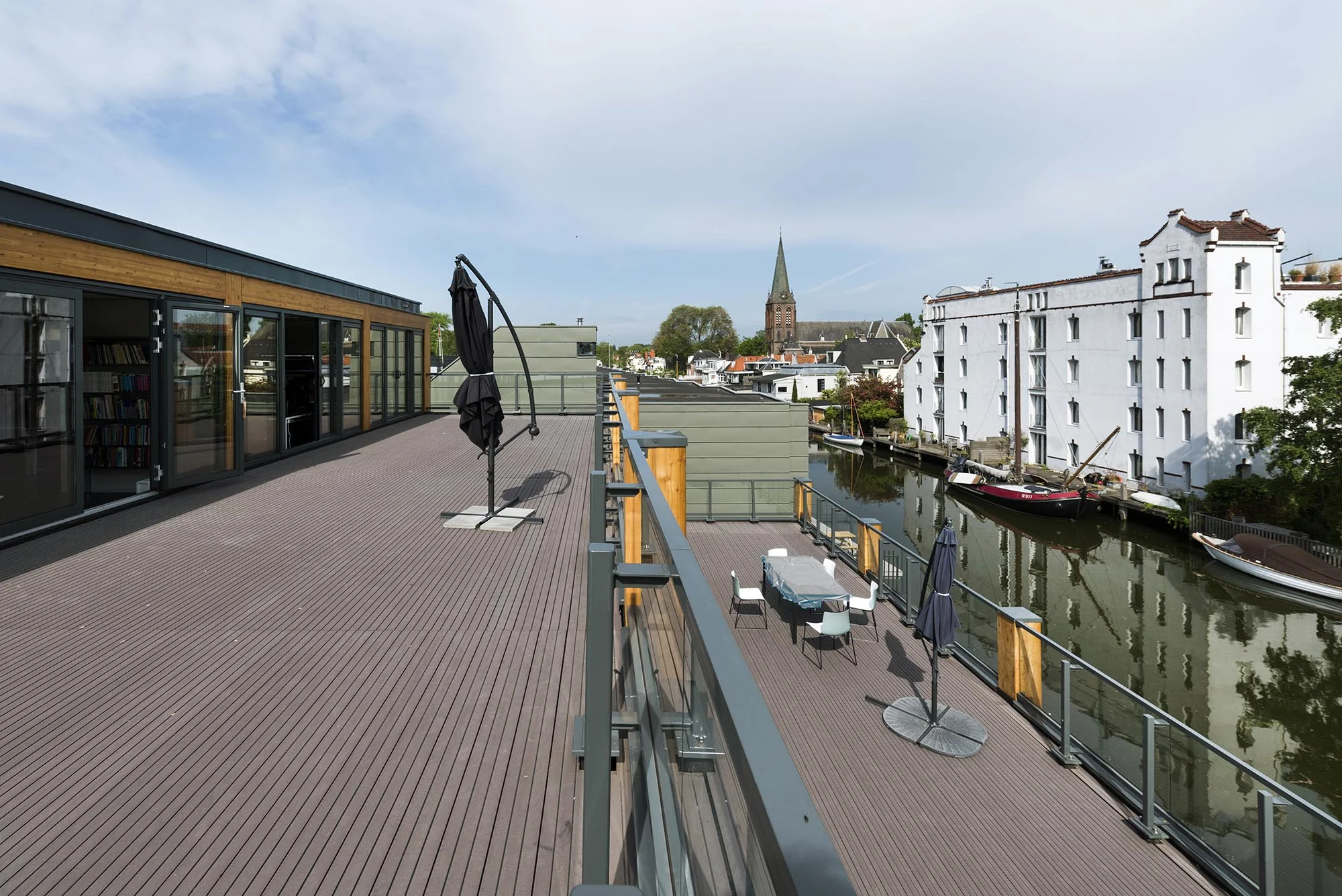 Ruim dakterras aan de Nieuwendammerkade met uitzicht op een kanaal, een witte pakhuizenrij en een kerktoren in de verte.