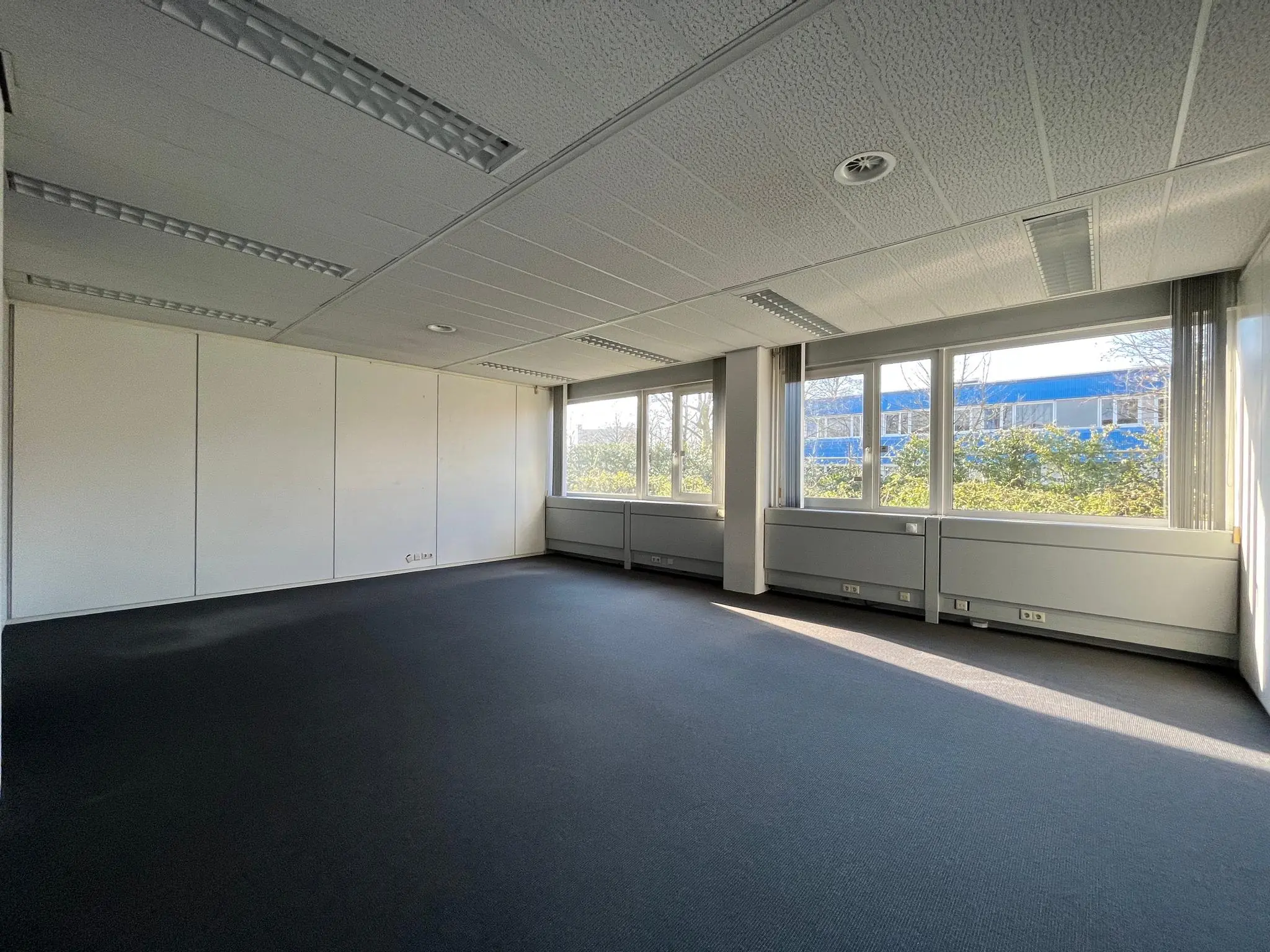 Lichte, lege kantoorruimte aan de Energieweg met grote ramen en uitzicht op een blauw kantoorgebouw.