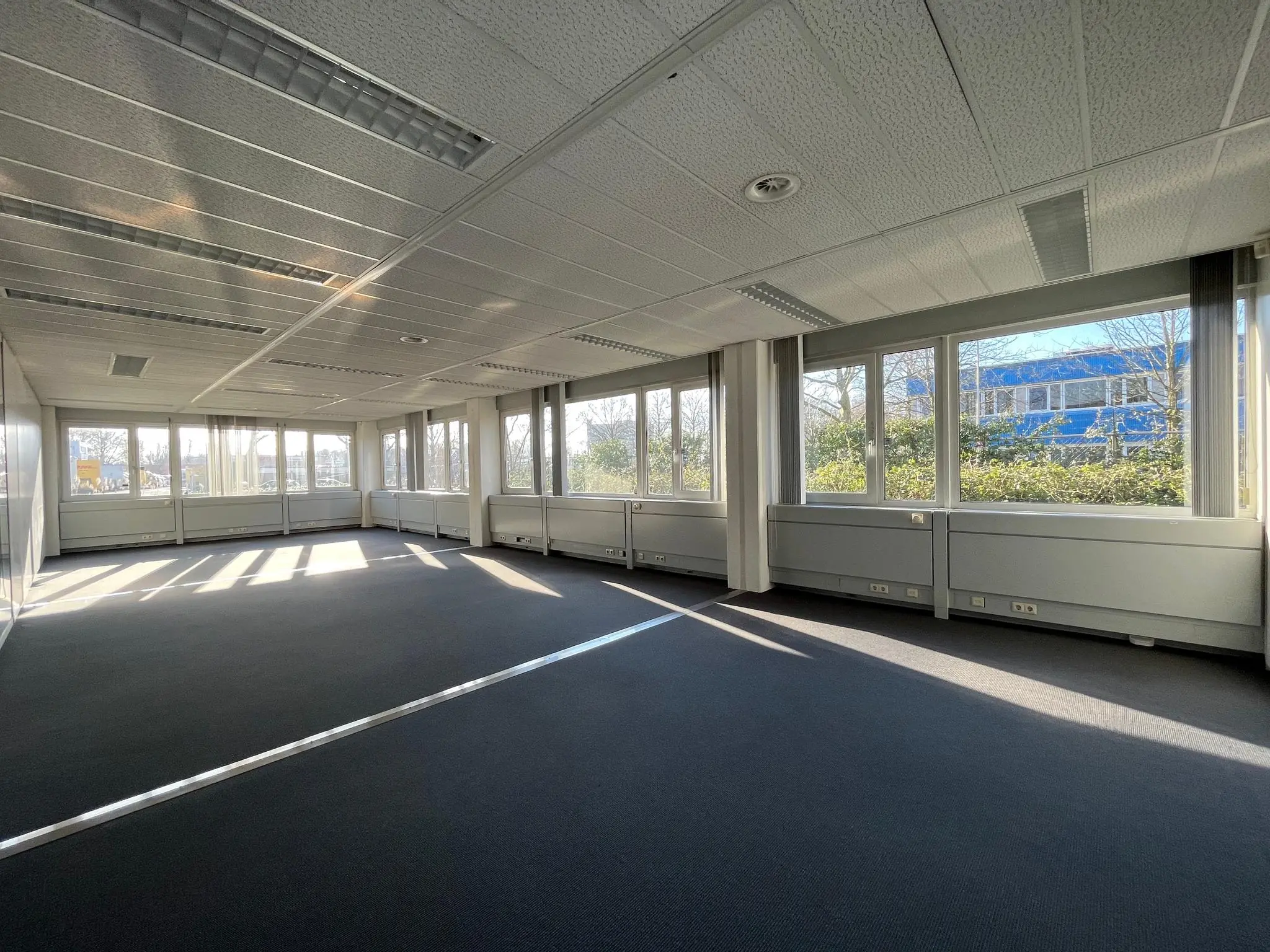 Lichte, lege kantoorruimte aan de Energieweg met grote ramen en uitzicht op een blauw gebouw.