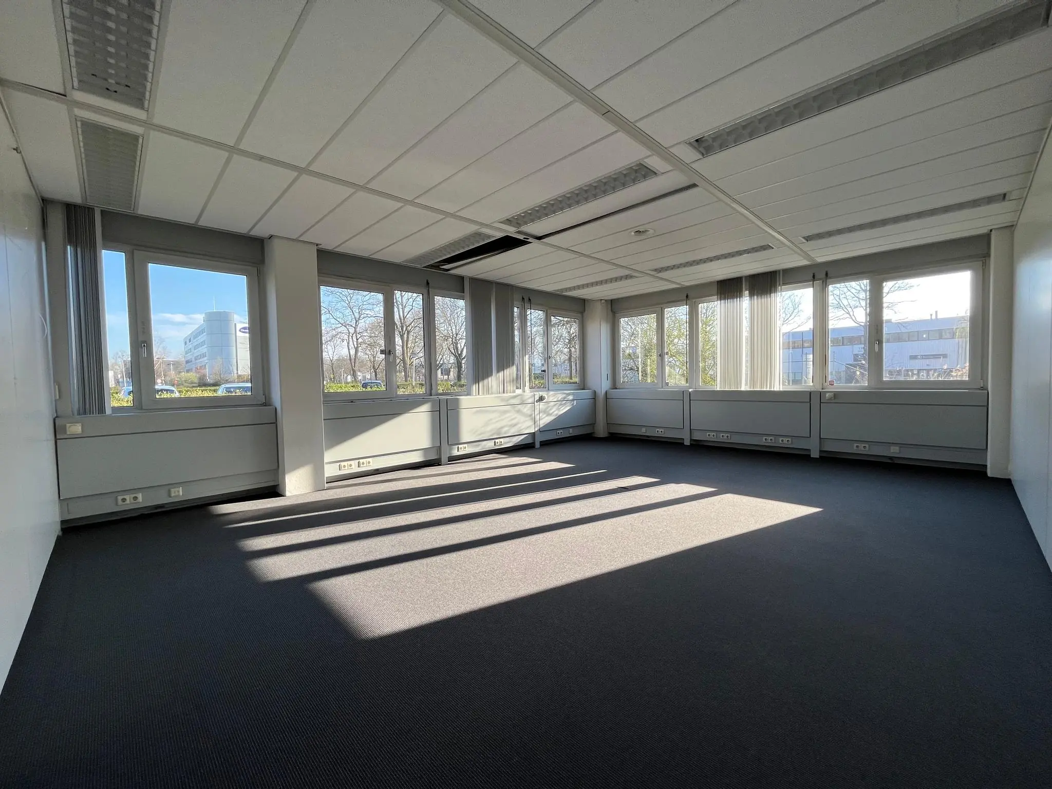 Licht en leeg kantoorpand met grote ramen aan de Energieweg, waar zonlicht lange schaduwen op de vloer werpt.