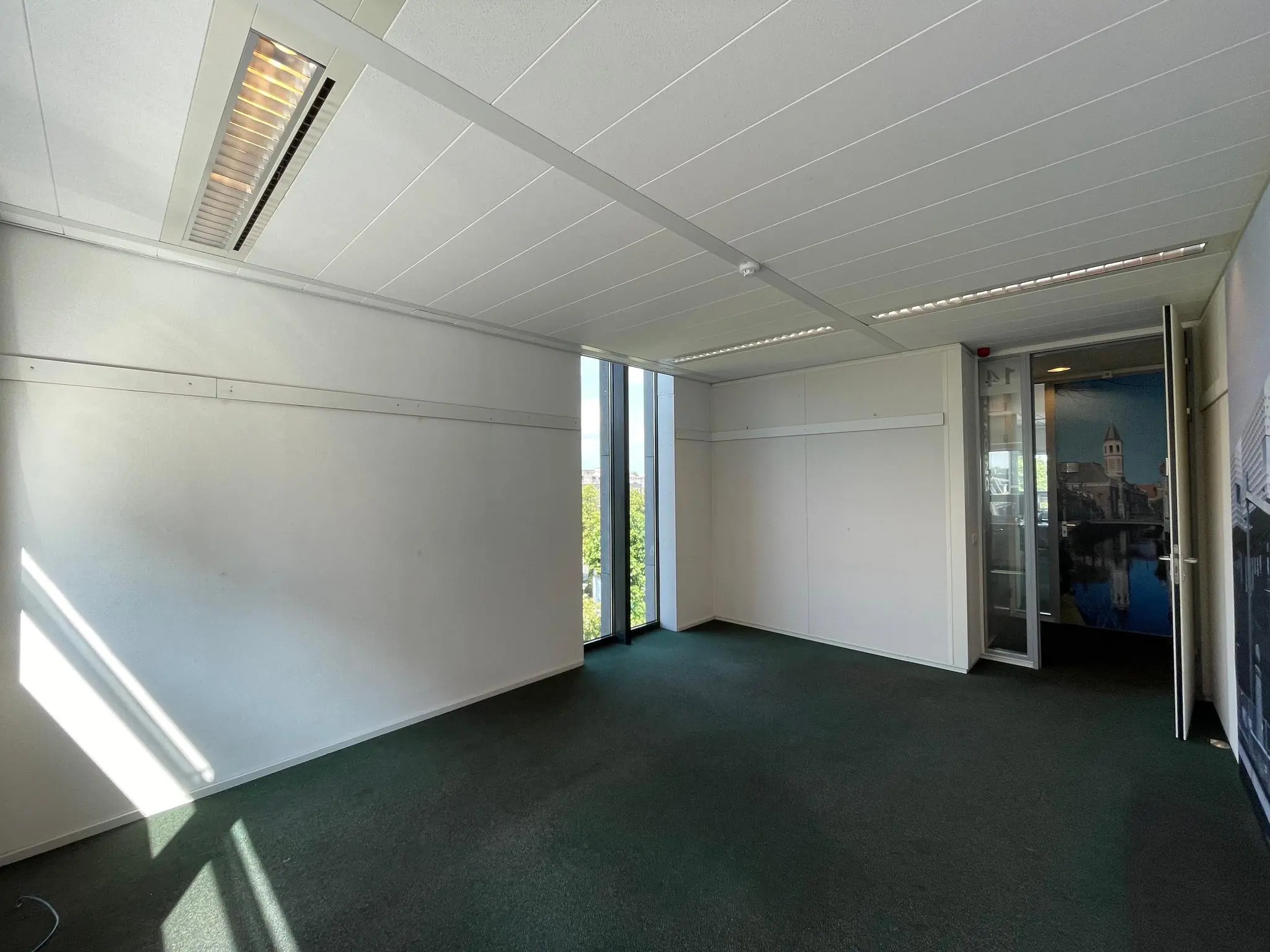 Leeg kantoorpand aan de Arnhemseweg met witte muren, groen tapijt en glazen deur met stadsfoto.