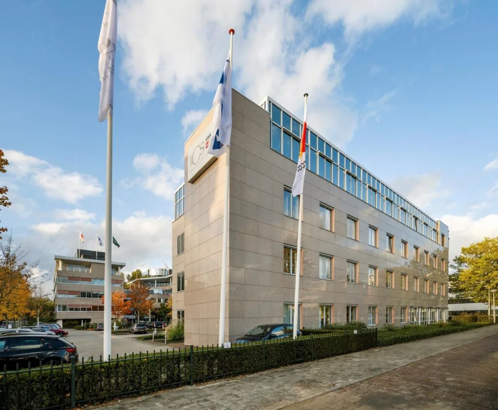 Kantoorpand van ICS Groep met vlaggen en parkeerterrein aan de voorzijde.