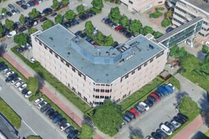 Luchtfoto van het kantoorgebouw 'De Wisselwerking' met omliggende parkeerplaatsen en groenstroken.