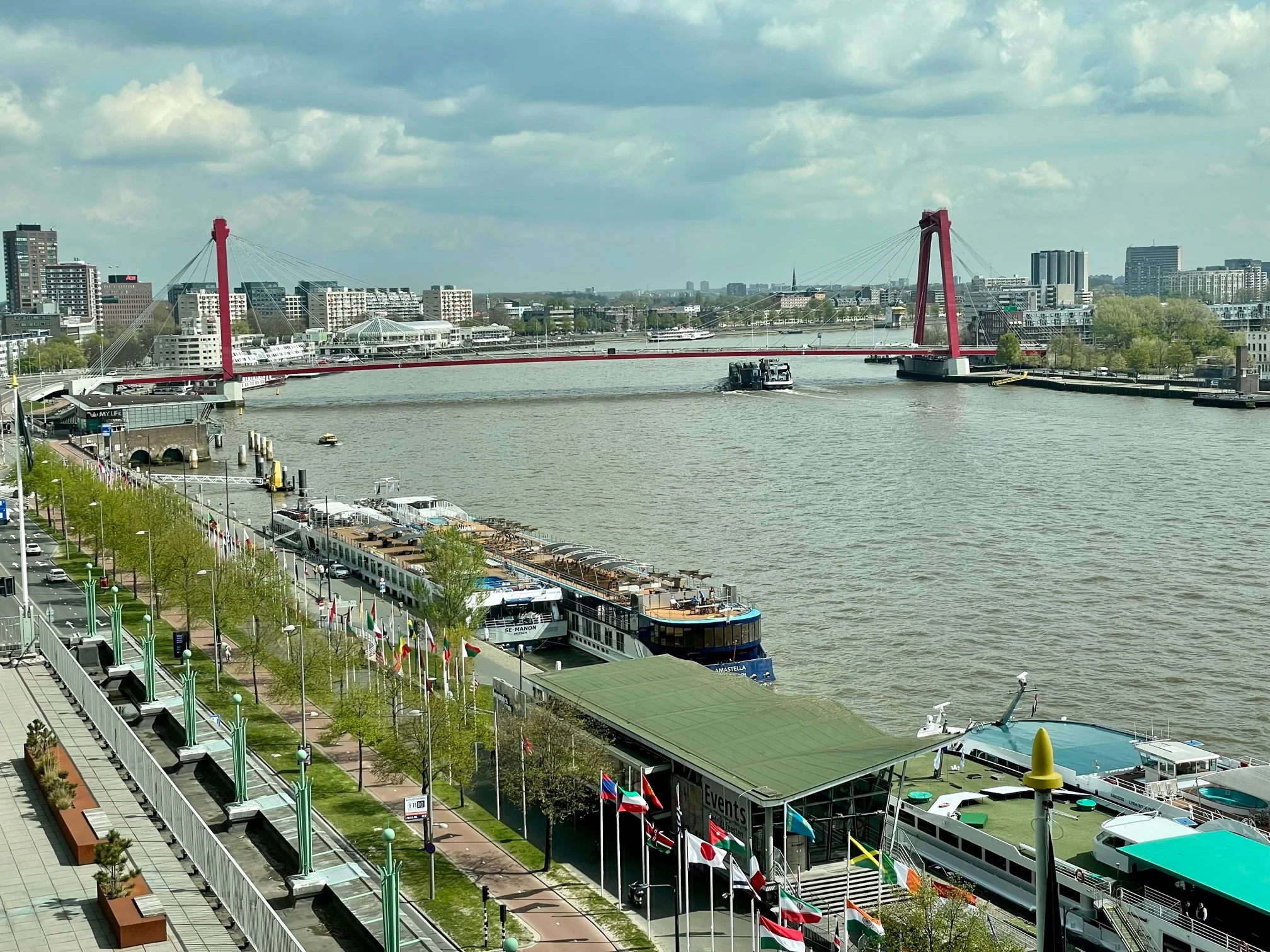 Uitzicht op de Boompjeskade in Rotterdam met aangemeerde riviercruiseschepen en de rode Willemsbrug over de Maas.