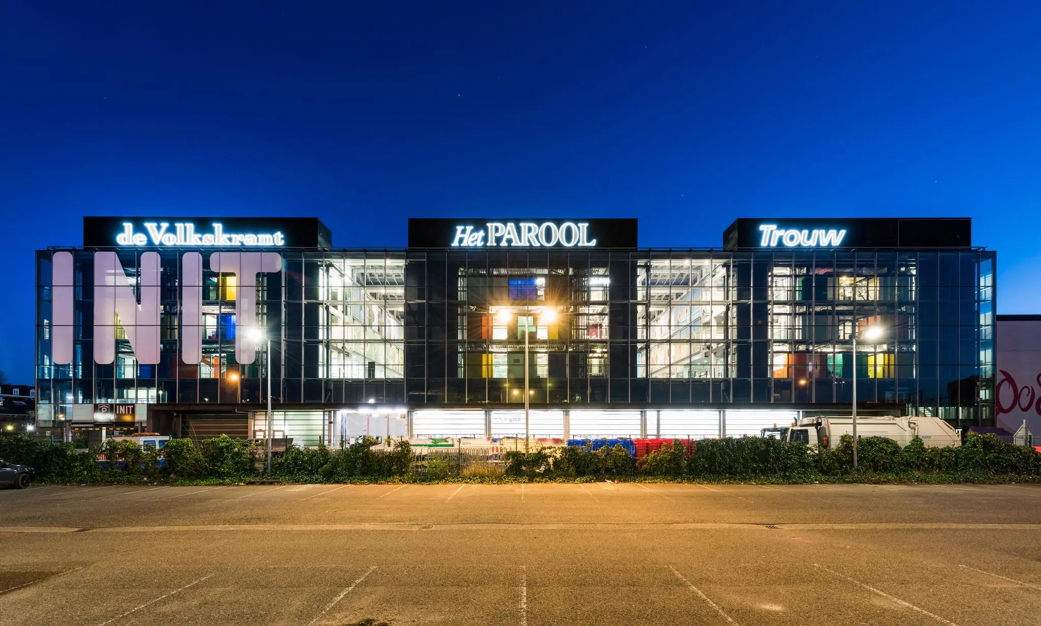 Verlichte gevel van het INIT-gebouw aan de Oostenburgermiddenstraat in Amsterdam, met logo’s van de kranten de Volkskrant, Het Parool en Trouw.