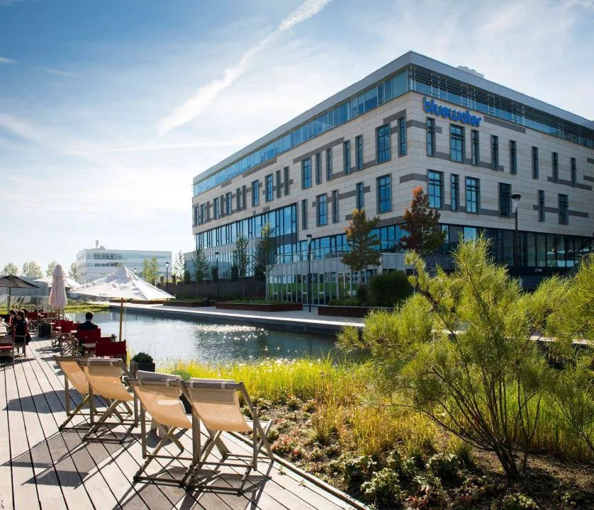 Moderne kantoorgebouwen aan het water met een terras en zitplaatsen onder parasols bij het Scorpius-complex.