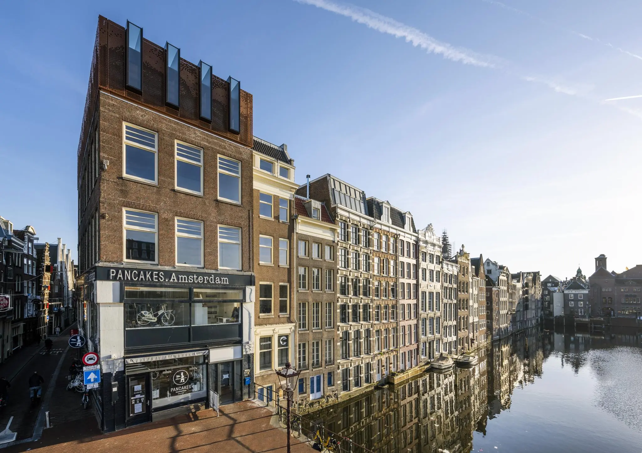 Zicht op de Prins Hendrikkade in Amsterdam met het restaurant PANCAKES Amsterdam en grachtenpanden langs het water.