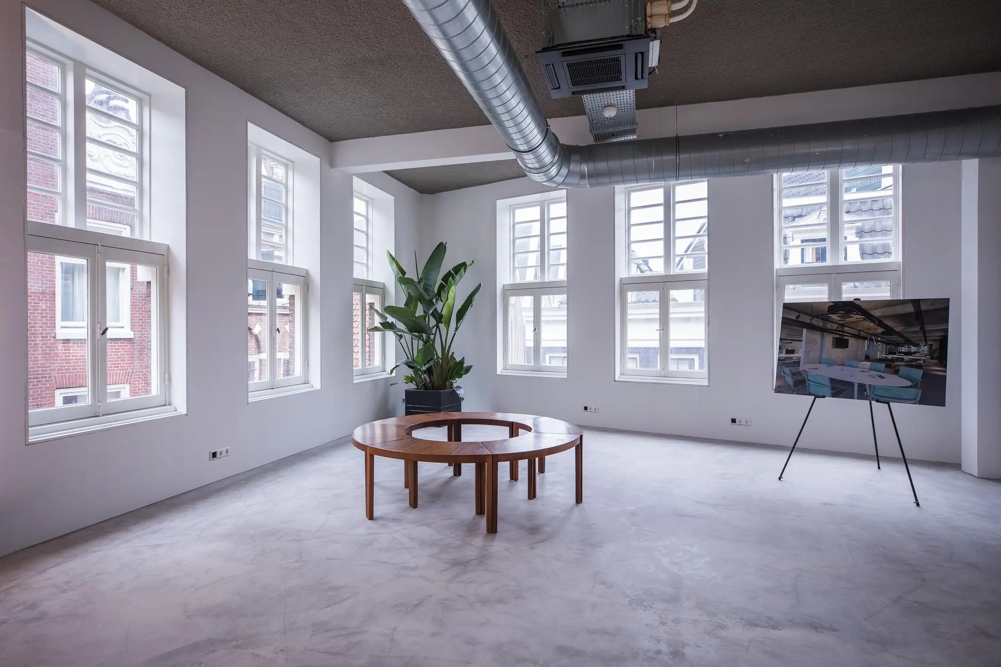 Licht en modern interieur aan de Prins Hendrikkade met ronde houten tafel, grote plant en presentatiebord.