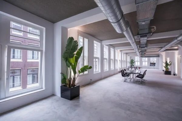 Ruim en modern kantoorinterieur aan de Prins Hendrikkade met grote ramen, betonnen vloer en industriële ventilatiebuizen.