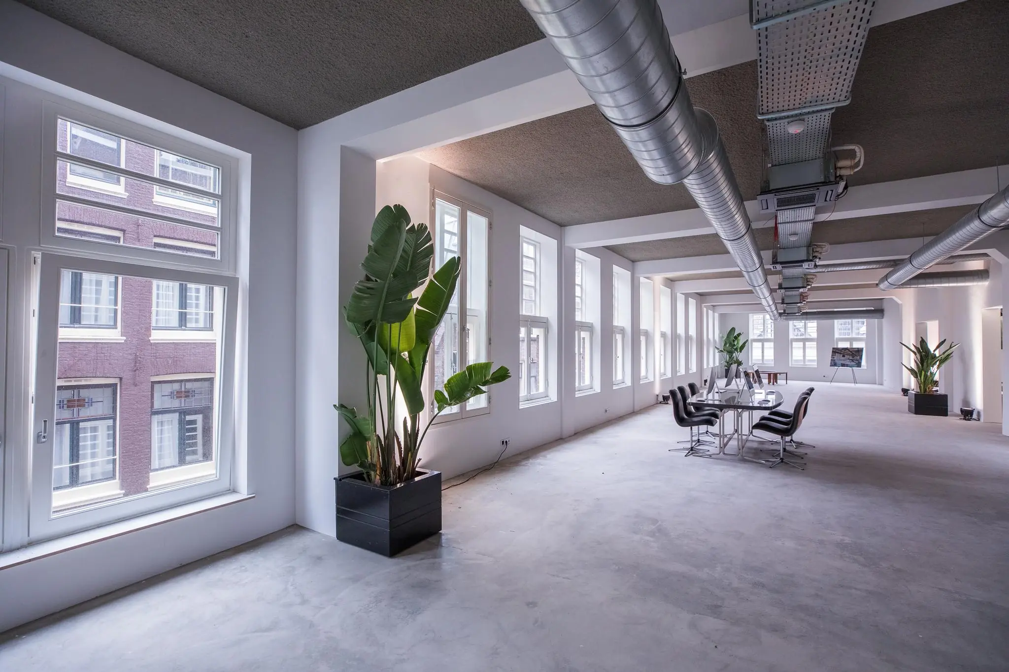 Ruim en modern kantoorinterieur aan de Prins Hendrikkade met grote ramen, betonnen vloer en industriële ventilatiebuizen.