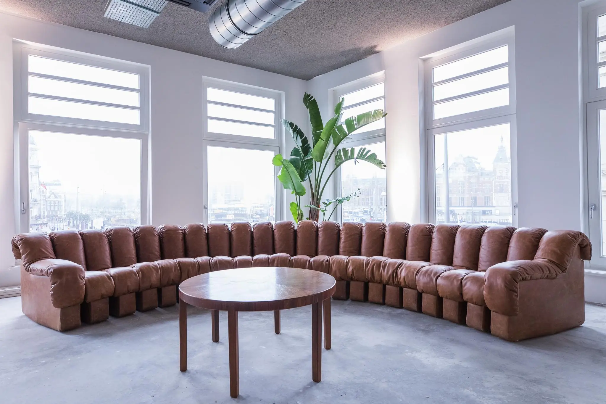Leren hoekbank met ronde houten tafel in een modern interieur aan de Prins Hendrikkade in Amsterdam.