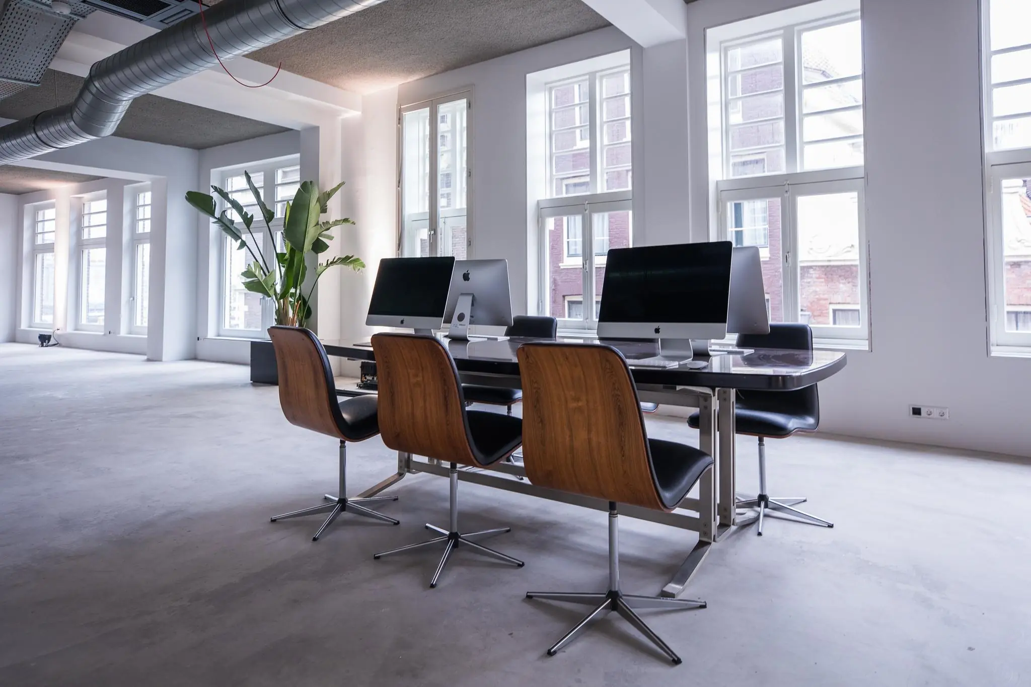 Moderne kantoorruimte aan de Prins Hendrikkade met een grote werktafel, iMacs en designstoelen bij hoge ramen.