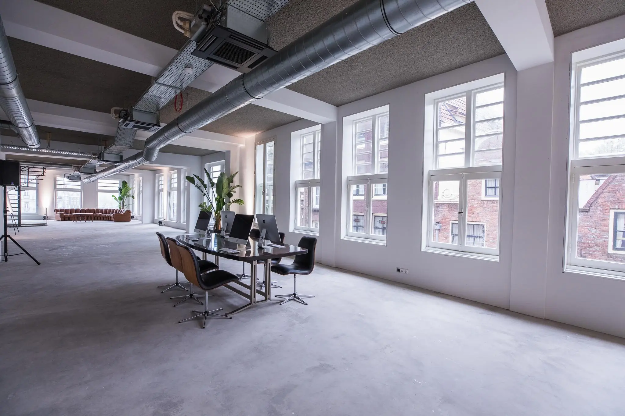 Modern industrieel kantoorinterieur aan de Prins Hendrikkade met grote ramen, een vergadertafel met iMacs en een loungehoek op de achtergrond.