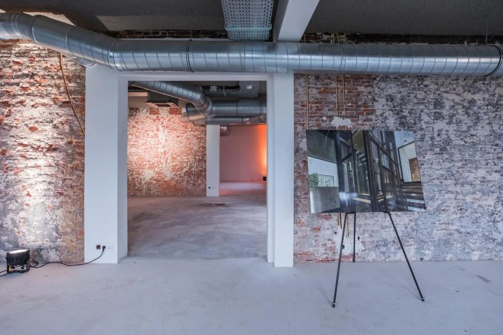 Industriële binnenruimte aan de Prins Hendrikkade met zicht op ruwe bakstenen muren, zichtbare ventilatiebuizen en een architectonisch ontwerp op een schildersezel.