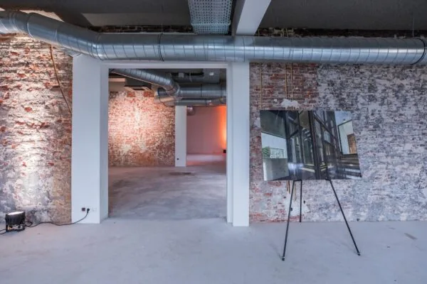 Industriële binnenruimte aan de Prins Hendrikkade met zicht op ruwe bakstenen muren, zichtbare ventilatiebuizen en een architectonisch ontwerp op een schildersezel.