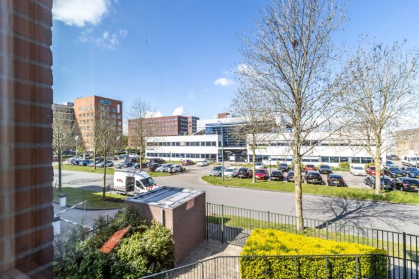 Uitzicht op het kantoorgebouw Veldzigt met parkeerterrein en omliggende kantoren op een zonnige dag.
