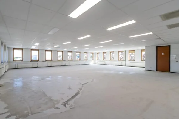 Leeg kantoorpand met systeemplafond, tl-verlichting en vele ramen aan beide zijden.