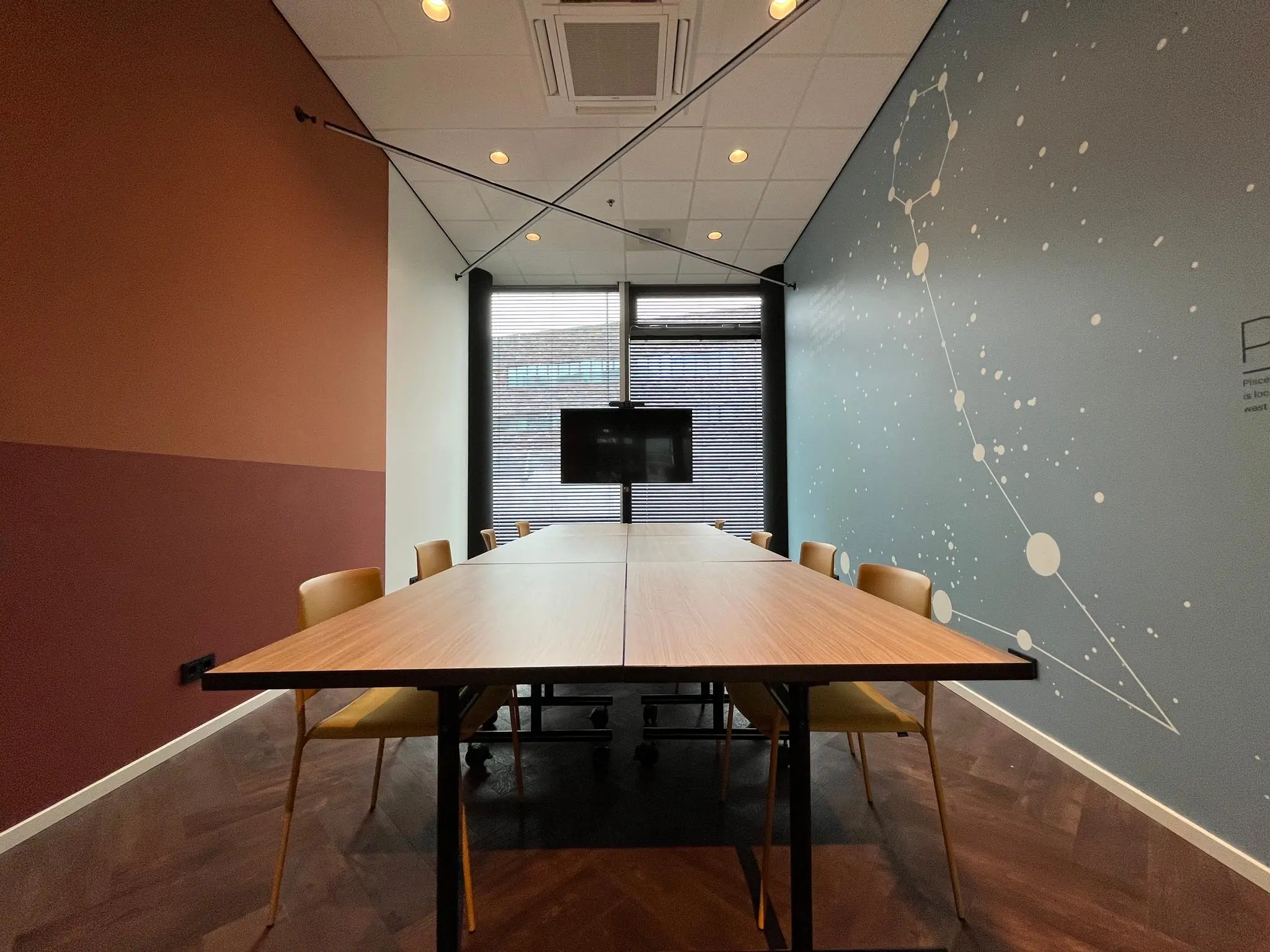 Vergaderruimte op het Herculesplein met houten tafel, gele stoelen en een wanddecoratie van sterrenbeelden.