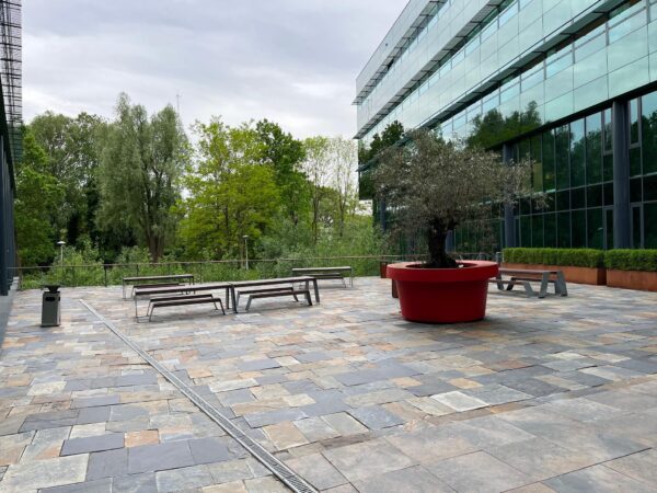 Buitenplein bij het Herculesplein met zitbanken, een grote rode plantenbak en modern kantoorgebouw met glazen gevel.