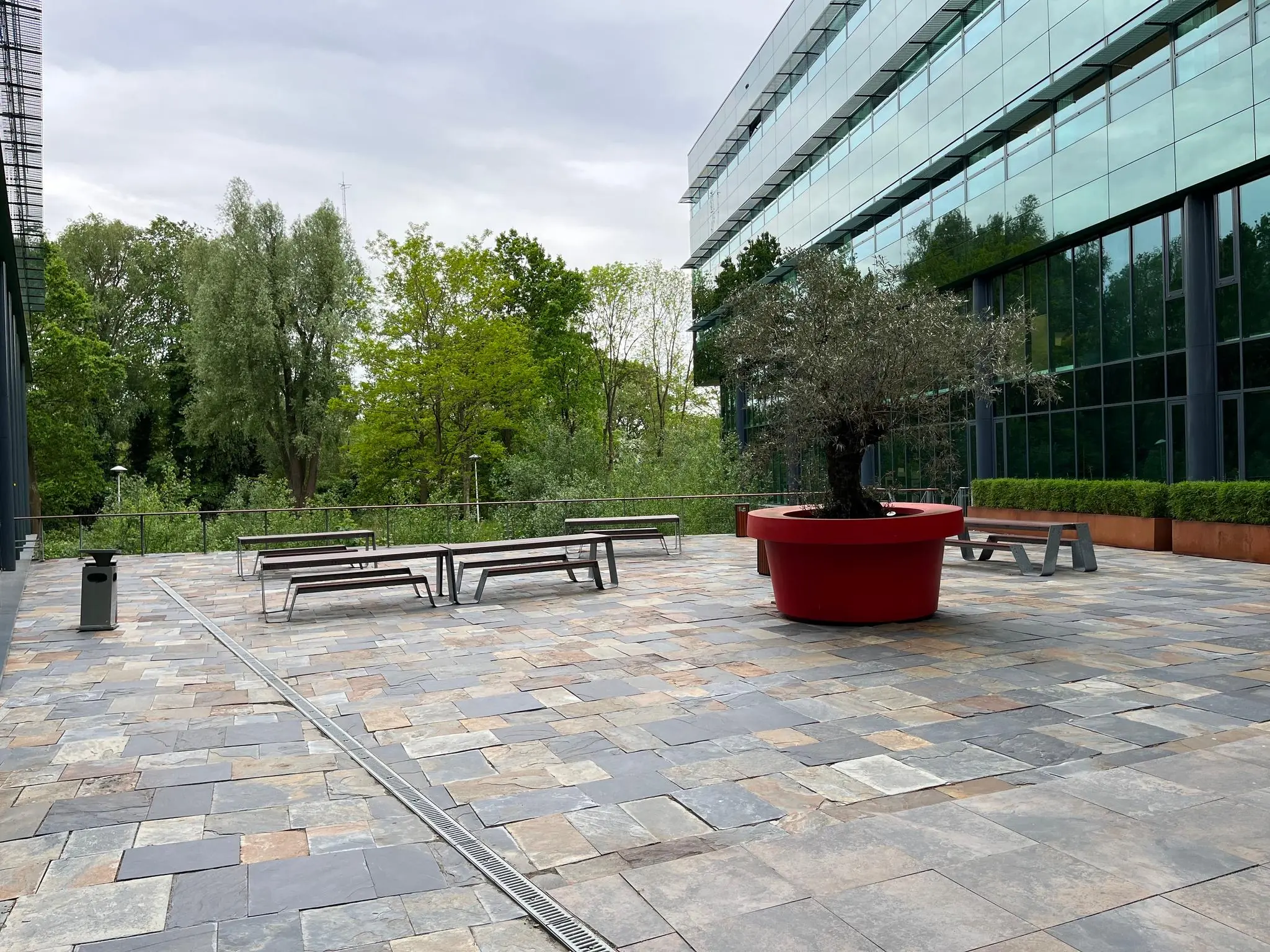 Buitenplein bij het Herculesplein met zitbanken, een grote rode plantenbak en modern kantoorgebouw met glazen gevel.