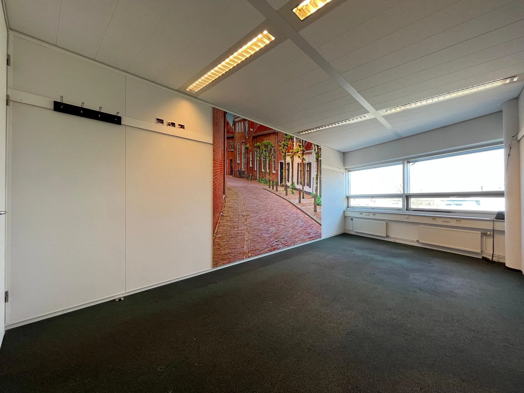 Leeg kantoor met tapijtvloer, grote ramen en een muurdecoratie van een straatbeeld in Arnhem.
