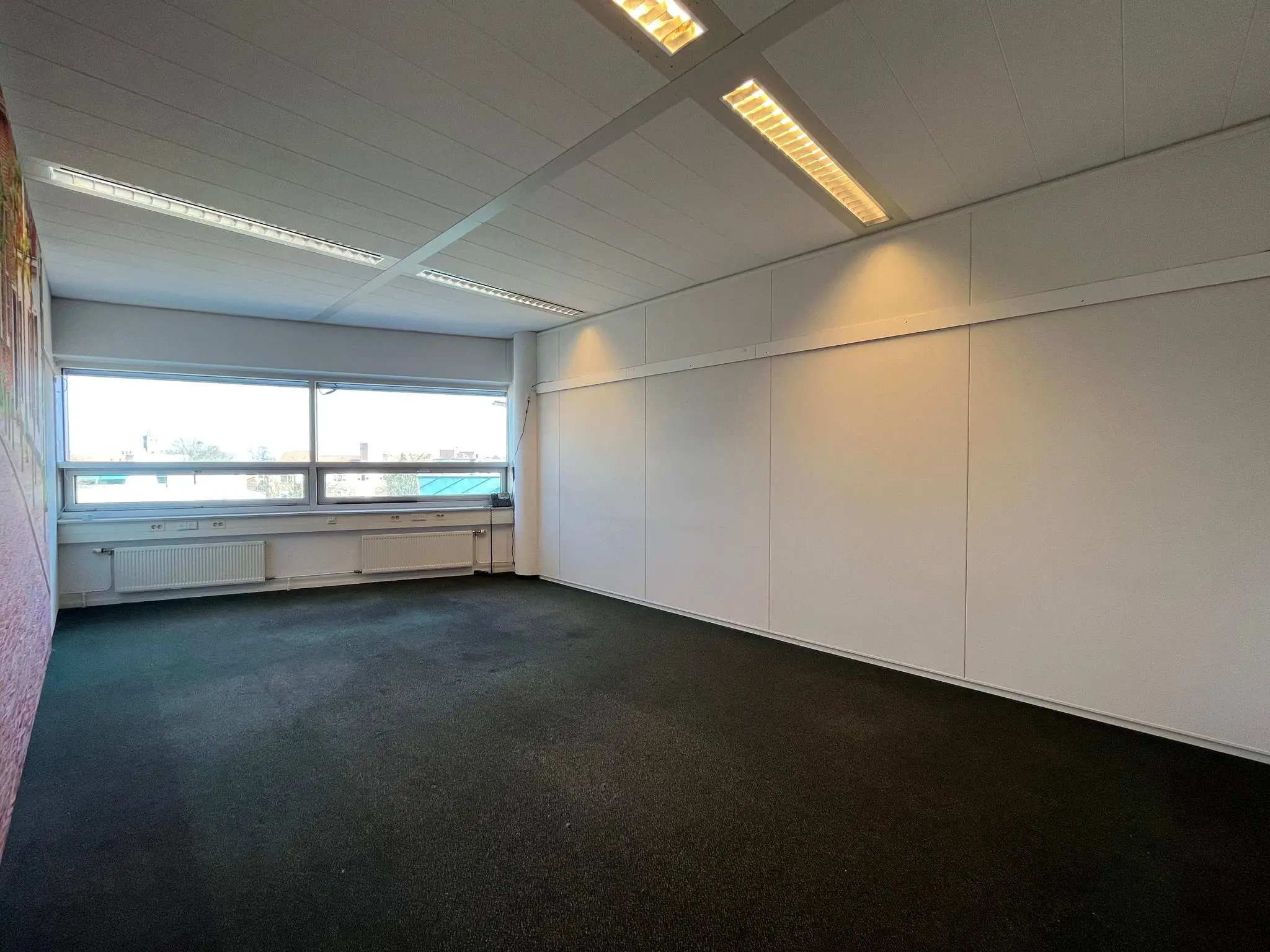 Leeg kantoor met wit plafond, grote ramen en donker tapijt aan de Arnhemseweg.