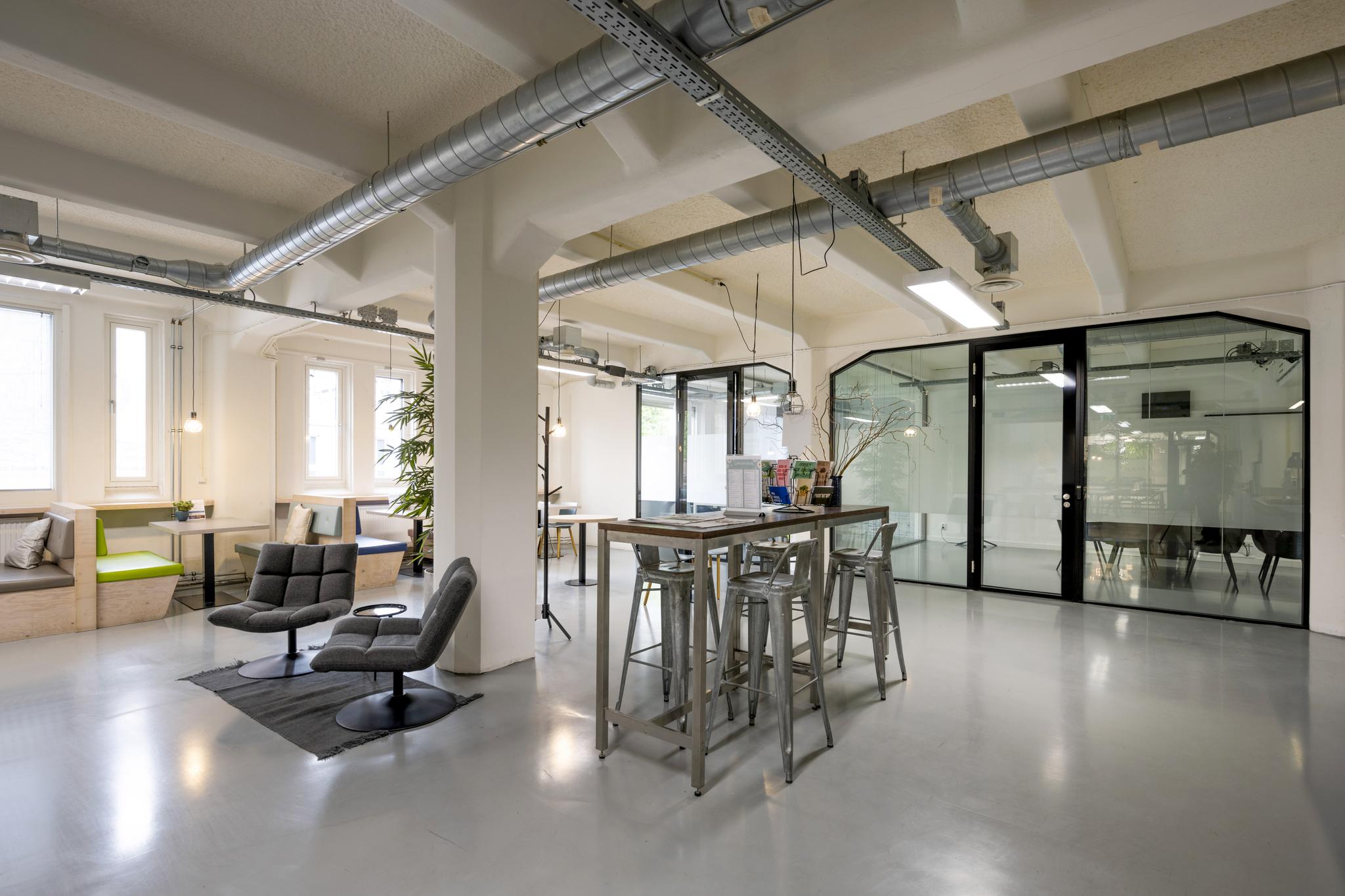 Modern ingericht kantoor met industriële uitstraling aan de Van Diemenstraat, met zitjes, hoge tafels en glazen vergaderruimte.