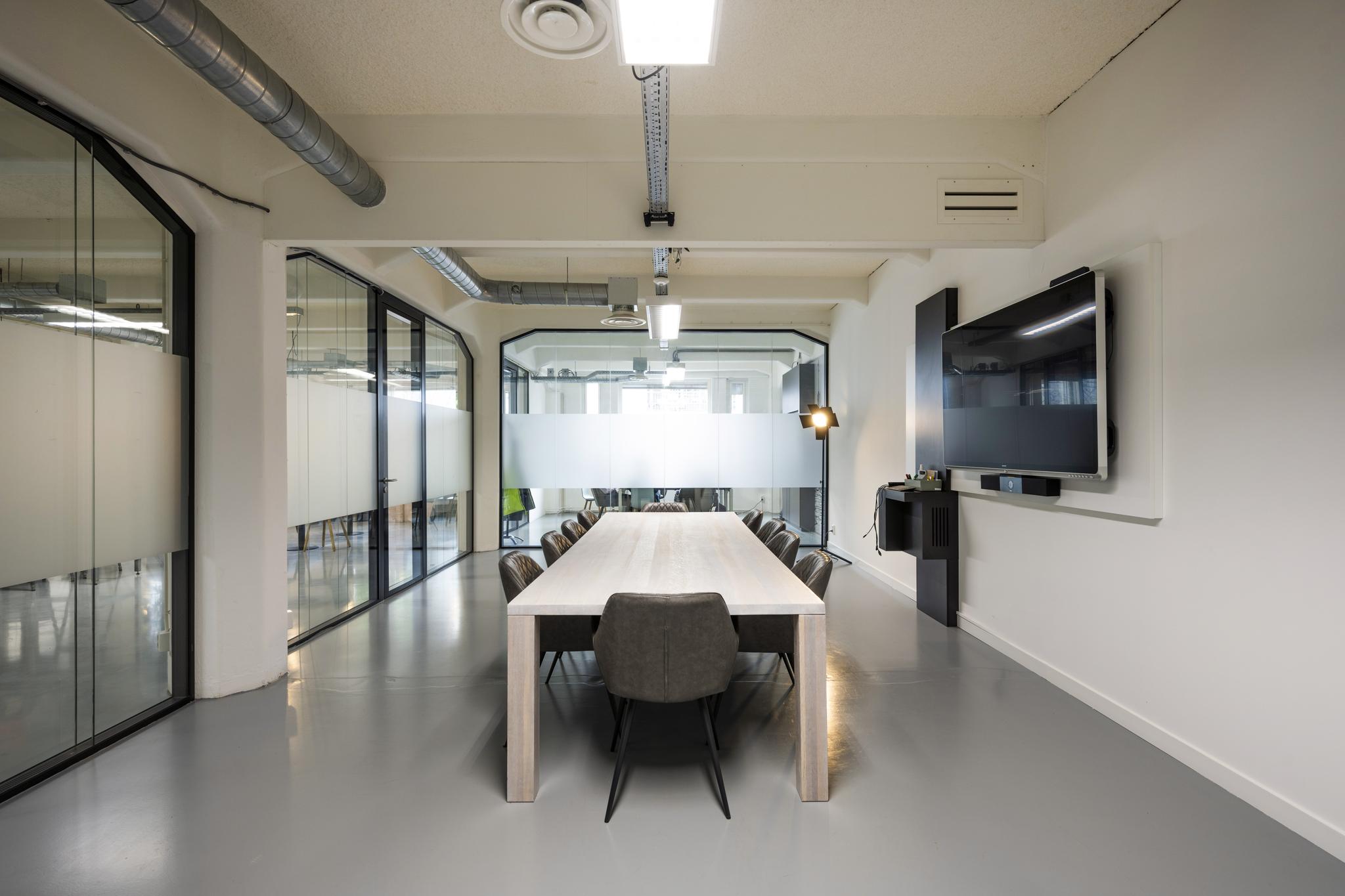 Moderne vergaderruimte aan de Van Diemenstraat met een lange tafel, leren stoelen en een groot digitaal presentatiescherm.