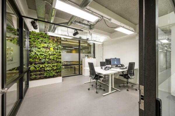 Modern kantoor aan de Van Diemenstraat met strakke werkplekken en een groene plantenwand.