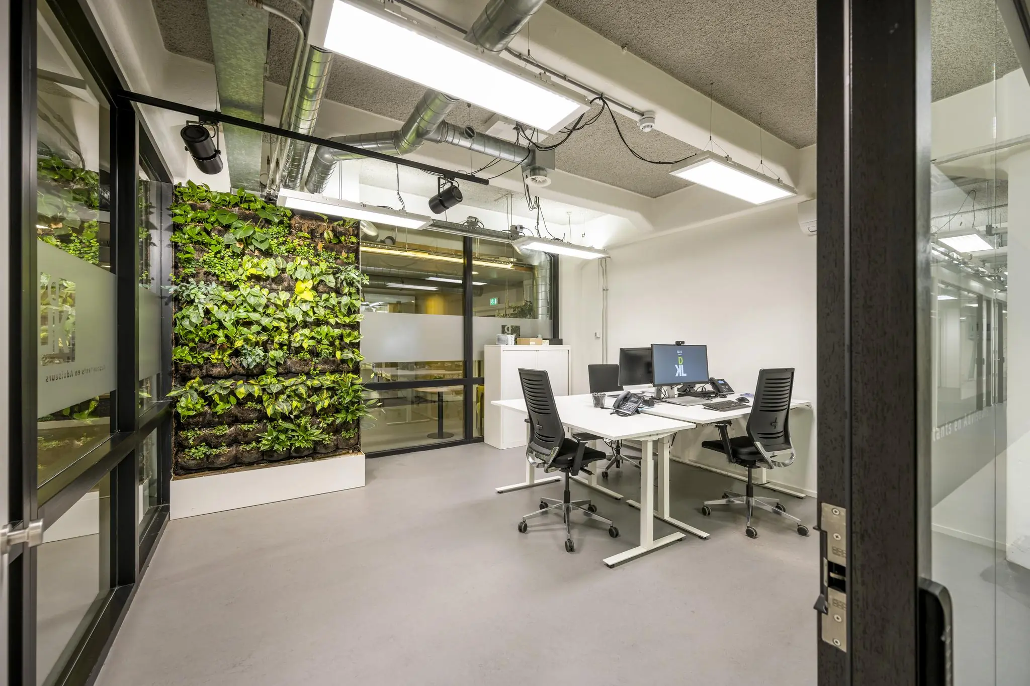 Modern kantoor aan de Van Diemenstraat met strakke werkplekken en een groene plantenwand.