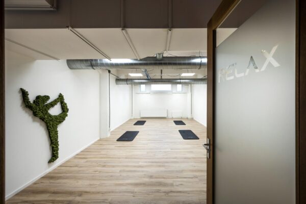 Minimalistische yogastudio aan de Van Diemenstraat met yogamatten op een houten vloer, een muurdecoratie van mos in yogahouding en een deur met het woord "RELAX".