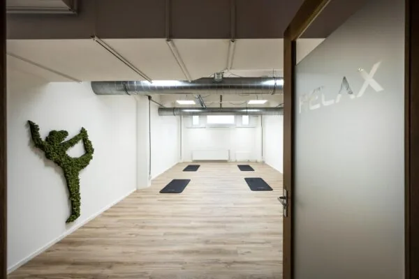 Minimalistische yogastudio aan de Van Diemenstraat met yogamatten op een houten vloer, een muurdecoratie van mos in yogahouding en een deur met het woord "RELAX".