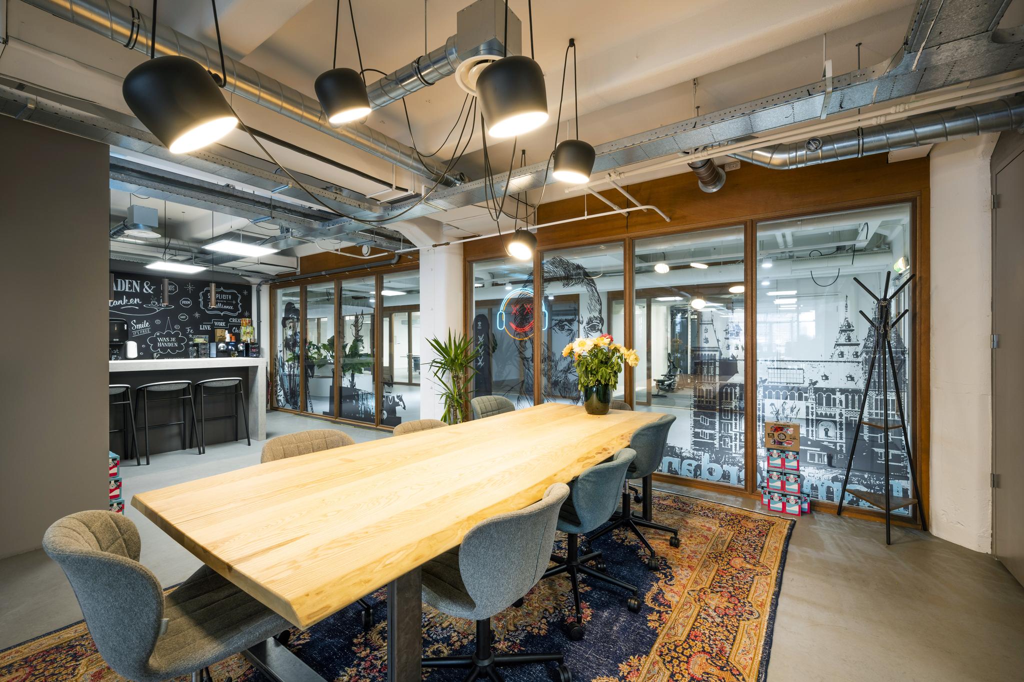 Moderne vergaderruimte aan de Van Diemenstraat met een houten tafel, designstoelen, hanglampen en glazen wanden met illustraties van Amsterdam.