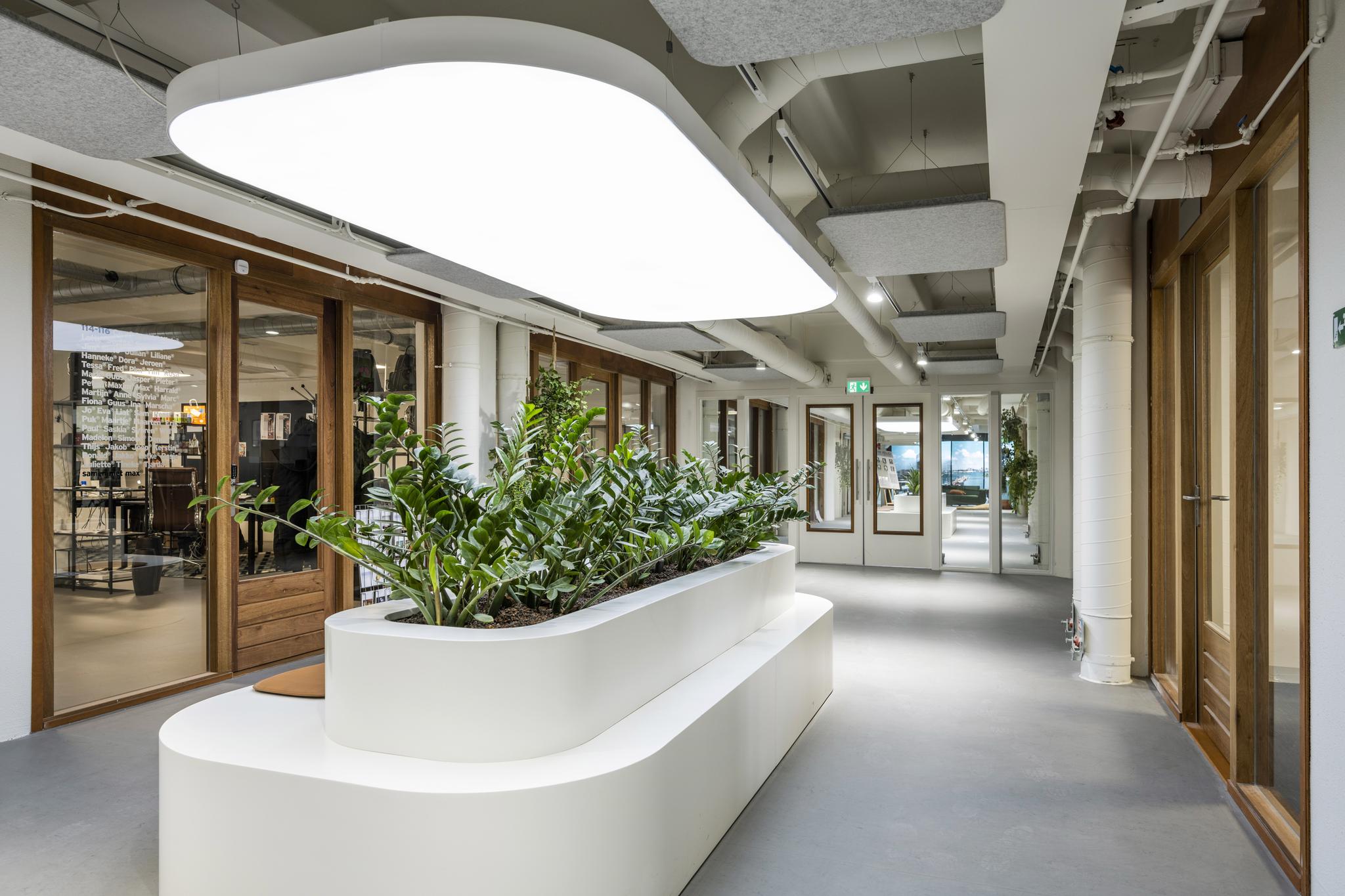 Moderne kantoorruimte aan de Van Diemenstraat met glazen wanden, houten details en een witte plantenbak met zitgelegenheid in het midden van de gang.
